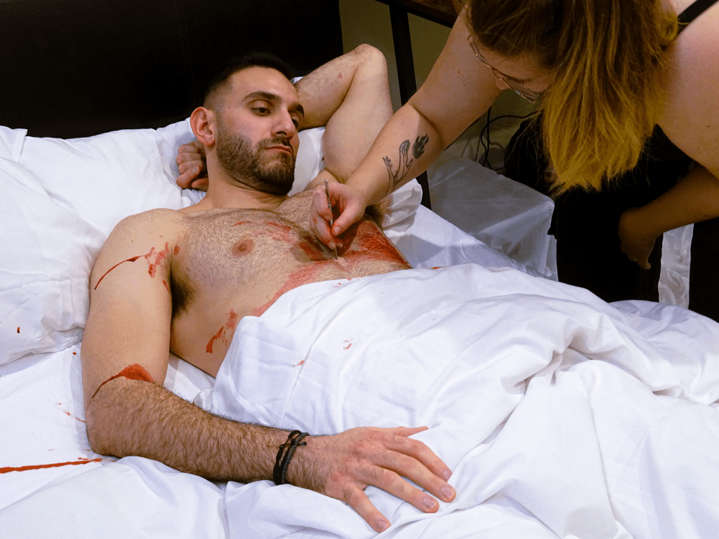 Actor lying on bed while makeup artist prepares him for a take.