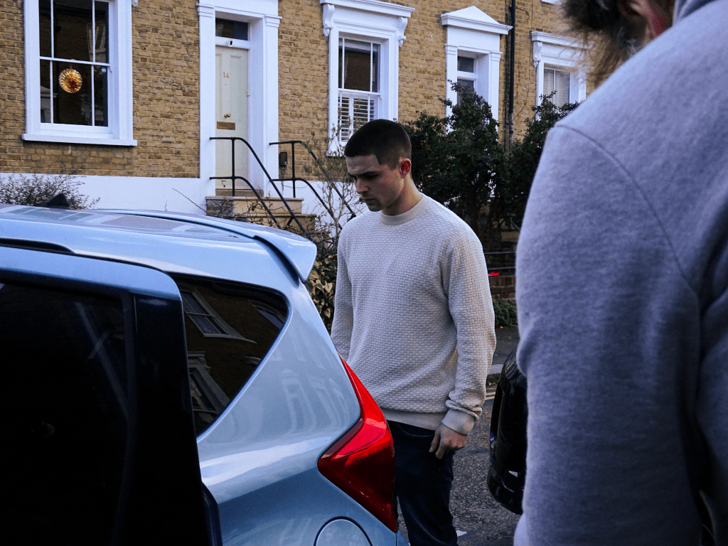 Actor standing behind car.