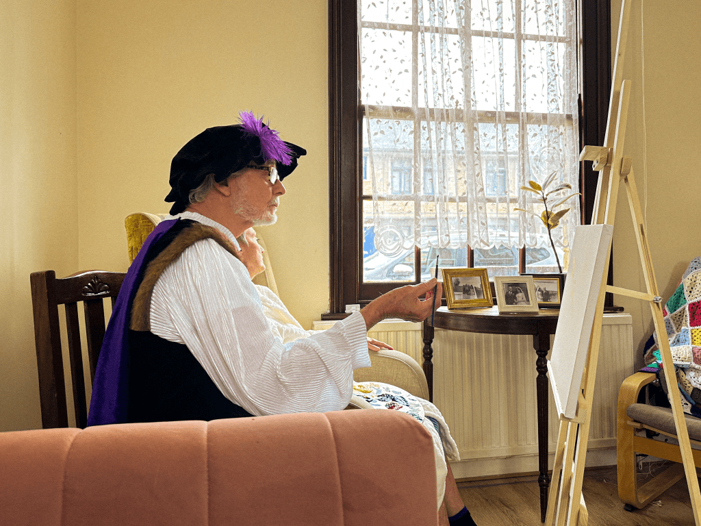 Actor holds a brush while staring at a blank canvas.
